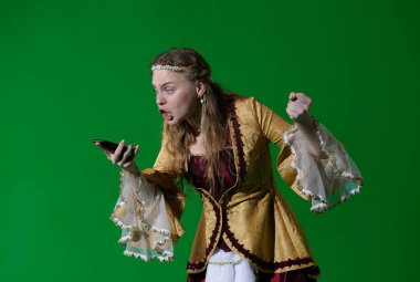 Tarihsel reklam konsepti. Krom anahtar yeşil ekran arka planda antik kıyafetli bir kadın. Rönesans elbisesi giymiş bir kadın elinde akıllı telefon ve ekrana bağıran yumruğunu yumruk için kaldıran kızgın bir kadın..