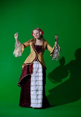 Tarihsel reklam konsepti. Krom anahtar yeşil ekran arka planda antik kıyafetli bir kadın. Rönesans kıyafetli, kulaklıklı, akıllı telefonlu, gülümseyen ve eğlenen bir kadın..