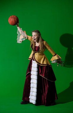 Tarihsel reklam konsepti. Krom anahtar yeşil ekran arka planda antik kıyafetli bir kadın. Rönesans elbisesi giymiş, heyecanlı yüzüyle basketbol topunu elinde tutmaya hazır bir kadın..
