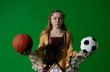 Tarihsel reklam konsepti. Krom anahtar yeşil ekran arka planda antik kıyafetli bir kadın. Rönesans elbisesi giymiş kafası karışmış bir kadın elinde basketbol topu ve elinde futbol topu tutuyor..