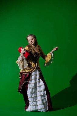 Tarihsel reklam konsepti. Krom anahtar yeşil ekran arka planda antik kıyafetli bir kadın. Rönesans elbisesi içinde kırmızı müzik hoparlörü tutan müzik dinleyen ve dans eden bir kadın..