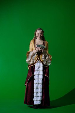 Tarihsel reklam konsepti. Krom anahtar yeşil ekran arka planda antik kıyafetli bir kadın. Rönesans elbiseli, gülen yüzlü para hayranı bir kadın. Nakit paralar..