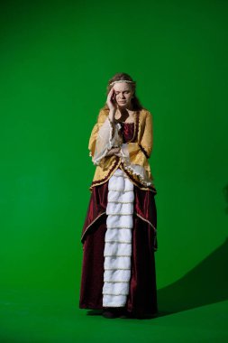 Tarihsel reklam konsepti. Krom anahtar yeşil ekran arka planda antik kıyafetli bir kadın. Rönesans elbisesi giymiş bir kadın baş ağrısı çekiyor. Acı dolu bir yüz ifadesi var. Masaj yapıyor..