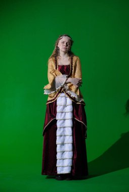 Tarihsel reklam konsepti. Krom anahtar yeşil ekran arka planda antik kıyafetli bir kadın. Rönesans elbisesi giymiş, yüzü negatif kuşkulu bir kadın kameraya bakıyor ve poz veriyor..