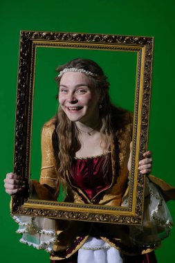 Tarihsel reklam konsepti. Krom anahtar yeşil ekran arka planda antik kıyafetli bir kadın. Rönesans elbisesi giymiş bir kadın elinde antika bir çerçeve ve kamera önünde portre resmi gibi poz veriyor..