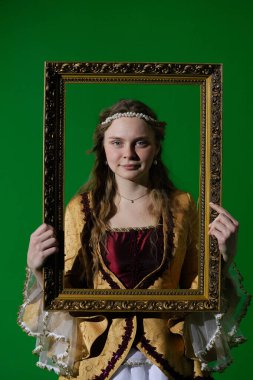 Tarihsel reklam konsepti. Krom anahtar yeşil ekran arka planda antik kıyafetli bir kadın. Rönesans elbisesi giymiş bir kadın elinde antika bir çerçeve ve kamera önünde portre resmi gibi poz veriyor..