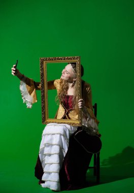 Tarihsel reklam konsepti. Krom anahtar yeşil ekran arka planda antik kıyafetli bir kadın. Rönesans elbisesi giymiş bir kadın resim yapmak için akıllı telefondan selfie çekiyor..