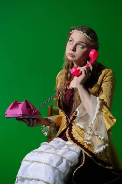 Tarihsel reklam konsepti. Krom anahtar yeşil ekran arka planda antik kıyafetli bir kadın. Rönesans elbisesi giymiş bir kadın oturmuş, pembe retro telefondan arıyor, ifadesini düşünüyor..