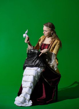 Tarihsel reklam konsepti. Krom anahtar yeşil ekran arka planda antik kıyafetli bir kadın. Rönesans elbisesi giymiş plastik çöp torbası tutan ve kağıt parçasına bakan bir kadın..