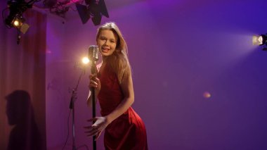 Profesyonel bir stüdyonun içinde. Işıklandırma ekipmanları ve siklonamayla fotoğraf çekimi stüdyosu. Ortadaki retro mikrofonda şarkı söyleyen kırmızı elbiseli kadın şarkıcı..