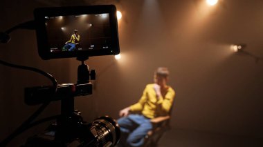 Profesyonel bir stüdyonun içinde. Aydınlatma ekipmanları ve siklonamayla fotoğraf çekimi için stüdyo, sandalyeye oturan kamera görüntüsü kayıt aktörüne yakın çekim.