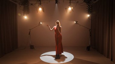 Profesyonel bir stüdyonun içinde. Işıklandırma ekipmanları ve siklonamayla fotoğraf çekimi stüdyosu. Ortadaki retro mikrofonda şarkı söyleyen kırmızı elbiseli kadın şarkıcı..