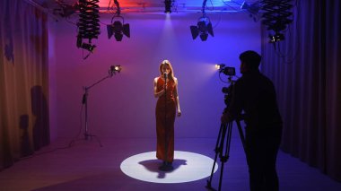 Profesyonel bir stüdyonun içinde. Işıklandırma ekipmanları ve siklonamayla fotoğraf çekimi stüdyoları, sahne arkasında neon ışıklı retro mikrofonla şarkı söyleyen kadın şarkıcılar..