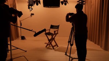 Profesyonel bir stüdyonun içinde. Aydınlatma ekipmanları ve siklonamayla fotoğraf çekimi stüdyoları, ışık ve kamerayı kapatan takım üyeleri, ortada yönetmen koltuğu..