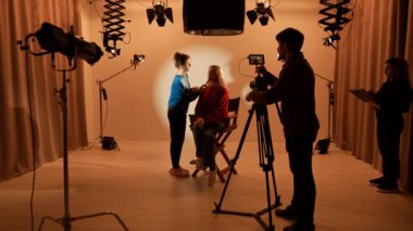 Profesyonel bir stüdyonun içinde. Aydınlatma ekipmanları ve siklonamayla fotoğraf çekimi stüdyoları, ışık ve kamera hazırlayan ekip üyeleri, kayıt yapmadan önce model makyajını tamir eden stilist.