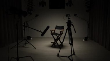 Profesyonel bir stüdyonun içinde. Aydınlatma ekipmanları ve siklonamayla fotoğraf çekimi stüdyosu, model aktris kameranın önündeki spot ışıklarının altında yönetmen koltuğunda oturuyor.