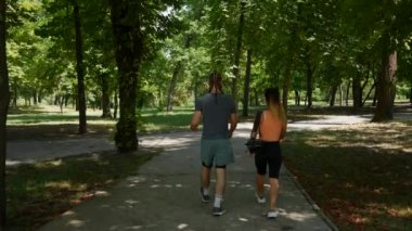 Spor giyim sektöründe gezintiye çıkmış genç bir çift. Şehir parkında yürüyen ve konuşan mutlu bir adamla bir kadının yavaş çekim görüntüleri. Boş zaman ve aktif yaşam tarzı kavramı. Arka plan.