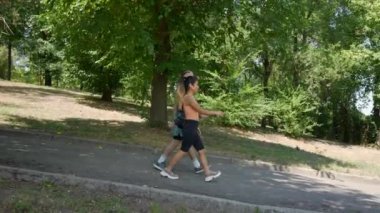 Spor giyim sektöründe gezintiye çıkmış genç bir çift. Şehir parkında yürüyen ve sohbet eden mutlu bir adamla bir kadının yavaş çekim görüntüleri. Yan görüş. Sağlıklı Yaşam Tarzı Konsepti.