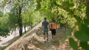 Spor giyim sektöründe gezintiye çıkmış genç bir çift. Şehir parkında yürüyen ve sohbet eden mutlu bir adamla bir kadının yavaş çekim görüntüleri. Arkadan bak. Sağlıklı Yaşam Tarzı Konsepti.
