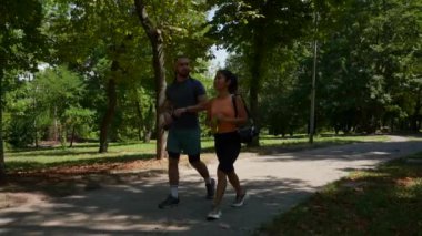 Spor giyim sektöründe gezintiye çıkmış genç bir çift. Parkta yürüyüp neşeyle sohbet eden mutlu bir adam ve kadının yavaş çekim görüntüleri. Boş zaman ve aktif yaşam tarzını kavra.