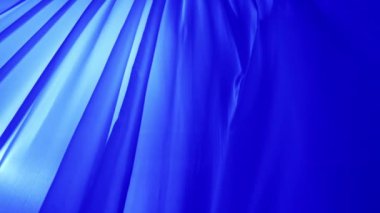 Rüzgarın savurduğu renkli tül kumaşlı pencereler. Açık bir pencereden süzülen şeffaf ipek perdeler mavi neon ışıkla renklendirilmiş, gölgeler tekstil üzerine yansıyor..