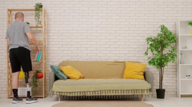 Kanepede oturan ve rahat bir oturma odasında kitap okuyan protez bacaklı bir adam. Kısıtlı hareketli adaptif yaşam biçimi kavramı.