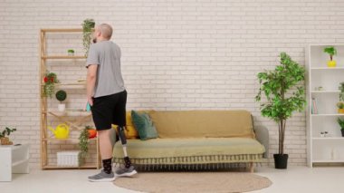 Protez bacaklı bir adam rahat bir oturma odasında yürüyor ve telefonla konuşuyor. Kısıtlı hareketli adaptif yaşam kavramı.