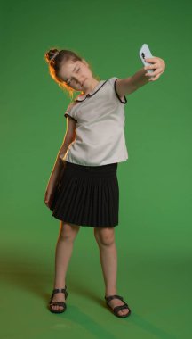 Stüdyoda poz veren liseli kız. Akıllı telefondan selfie çeken genç bir kız. Krom anahtar yeşil ekran arka planında izole edilmiş. Çalışma alanı modeli. Eğitim reklam kavramı.