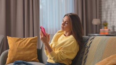 Kadın evde boş vakit geçiriyor. Genç bir kadın bütün gününü evde, oturma odasındaki kanepede oturarak geçiriyor. Elinde akıllı telefonları tutuyor, sosyal medyayı izliyor, tarafsız bir ifade takınıyor..