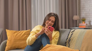 Kadın evde boş vakit geçiriyor. Genç bir kadın bütün gününü evde, oturma odasındaki kanepede oturarak geçiriyor. Akıllı telefondan mesaj atıyor ve cevap alıyor. Mutlu bir ifade..