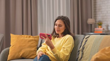 Kadın evde boş vakit geçiriyor. Genç bir kadın bütün gününü evinde, oturma odasındaki kanepede oturarak, elinde akıllı telefonuyla video izleyerek ve gülümseyerek geçiriyor..