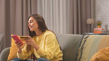 Kadın evde boş vakit geçiriyor. Genç bir kadın bütün gününü evinde, oturma odasındaki kanepede oturarak geçiriyor. Akıllı telefonunda kart numarası yazıyor. İnternetten alışveriş yapıyor..