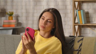 Kadın evde boş vakit geçiriyor. Genç bir kadın bütün gününü evde, oturma odasındaki kanepede oturarak geçiriyor. Elinde akıllı telefonları tutuyor, sosyal medyayı izliyor, tarafsız bir ifade takınıyor..