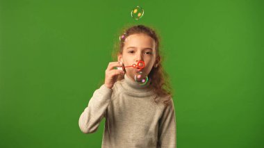 Children emotions concept. Little girl blowing in soap bubble stick maker, bubbles flying around, positive expression, isolated on chroma key green screen studio background mockup. clipart