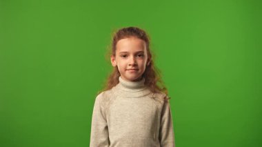 Çocuk duyguları konsepti. Tişörtlü küçük kız kameraya bakıyor ve gülümsüyor. Renkli yeşil ekran stüdyo arka planında izole edilmiş..
