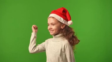 Çocuk duyguları konsepti. Noel Baba şapkalı gülümseyen kız kameraya dans ediyor, pozitif ifade, krom anahtar yeşil ekranda izole edilmiş arka plan modeli..