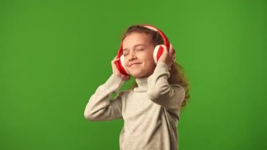 Çocuk duyguları konsepti. Kulaklıkla müzik dinleyen ve dans eden küçük bir kız çocuğu, pozitif ifade, krom anahtar yeşil ekranda izole edilmiş arka plan modeli..