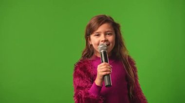 Çocuk duyguları konsepti. Gülümseyen kız çocuğu karaoke mikrofonunda şarkı söylüyor, pozitif ifade, krom anahtar yeşil ekranda izole edilmiş arka plan modeli..