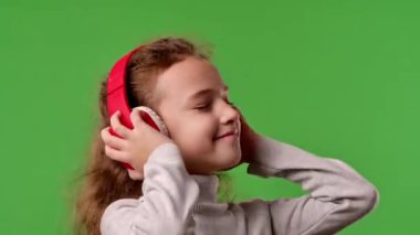 Çocuk duyguları konsepti. Kulaklıkla müzik dinleyen ve dans eden küçük bir kız çocuğu, pozitif ifade, krom anahtar yeşil ekranda izole edilmiş arka plan modeli..