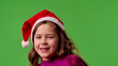 Çocuk duyguları konsepti. Noel Baba şapkalı gülümseyen kız kameraya şarkı söylüyor, pozitif ifade, krom anahtar yeşil ekranda izole edilmiş arka plan modeli..