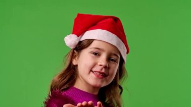 Çocuk duyguları konsepti. Noel Baba şapkalı, gülümseyen bir kız çocuğu hava öpücüğü verir ve gülümser, olumlu ifade, krom anahtar yeşil ekran arka plan modelinde izole edilmiş..