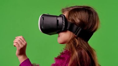 Çocuk duyguları konsepti. Sanal gerçeklik gözlüklü bir kız çocuğu sanal ekran menüsüne tıklayarak, yakınlaştırarak ve tıklayarak, krom anahtar yeşil ekran stüdyo arka planında izole edilmiş..