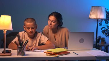 Bir öğrenci bir odada bir masada oturur ve ev ödevini yapar. Bir genç akşam karanlık bir odada ders çalışıyor ve annesi onun ev ödevini yapmasına yardım ediyor. Eğitim ve öğrenim kavramı.