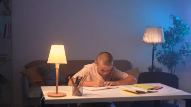 Bir okul çocuğu bir odada bir masada oturup ödev yapıyor. Genç bir çocuk ödevini bir defterde dikkatlice yapıyor. Eğitim ve öğrenim kavramı.