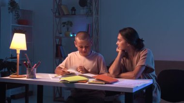Bir öğrenci bir odada bir masada oturur ve ev ödevini yapar. Bir genç akşam karanlık bir odada ders çalışıyor ve annesi onun ev ödevini yapmasına yardım ediyor. Eğitim ve öğrenim kavramı.