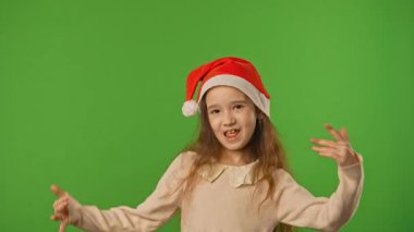 Çocuk duyguları konsepti. Noel Baba şapkalı küçük kız kamerada şarkı söylüyor, pozitif ifade, yeşil ekranda izole edilmiş arka plan modeli..