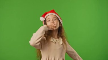 Çocuk duyguları konsepti. Noel Baba şapkalı küçük kız, hava öpücüğü ve gülücükler saçar, pozitif ifade, krom anahtar yeşil ekranda izole edilmiş arka plan modeli..