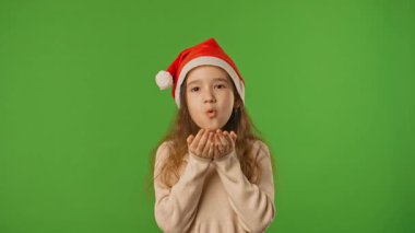 Çocuk duyguları konsepti. Noel Baba şapkalı küçük bir kız çocuğu karları uçurur ve etrafına bakar, pozitif ifade, krom anahtar yeşil ekranda izole edilmiş arka plan modeli..