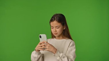 Çocuk duyguları konsepti. Akıllı telefon ve daktilo tutan Asyalı kız çocuğu, sosyal medyada kayan, pozitif ifade, krom anahtar yeşil ekran arka plan modelinde izole edilmiş.
