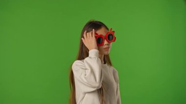 Çocuk duyguları konsepti. Asyalı kız çocuğu kameraya poz veriyor, kırmızı elma gözlüğü takıyor, pozitif ifade, krom anahtar yeşil ekran arka plan modelinde izole edilmiş..